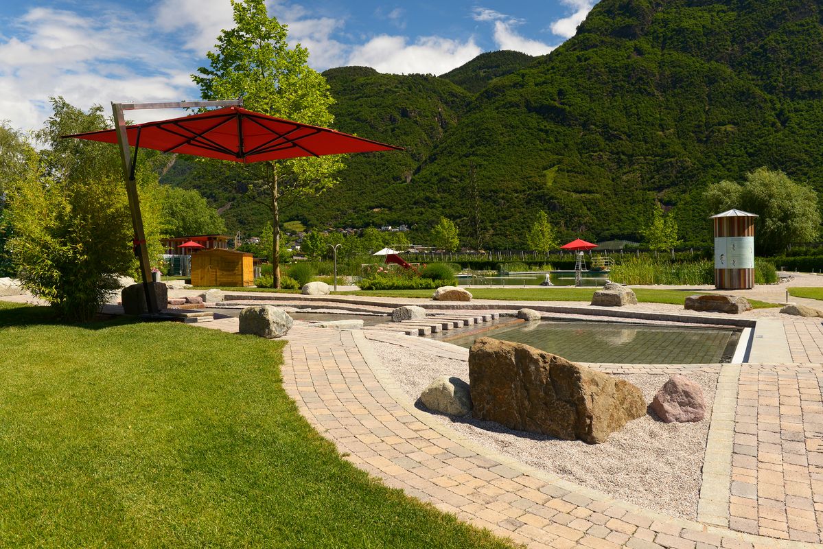 Area naturale per bambini con pietre, acqua bassa, prato e ombrellone rosso